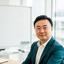 David Chen seated in a bright office beside a whiteboard of product notes